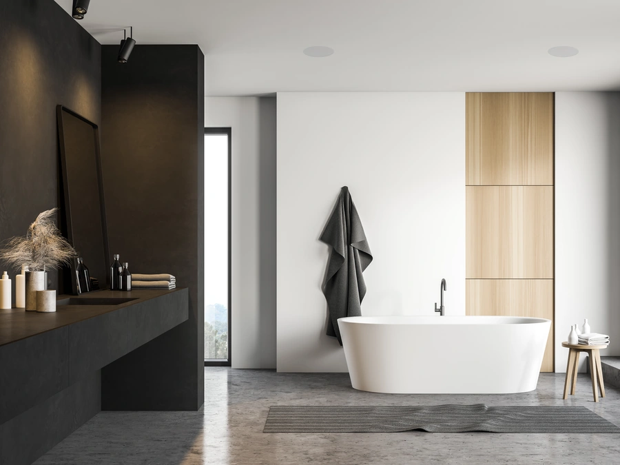 A dark stone bathroom with a freestanding bath and a speaker set into the ceiling