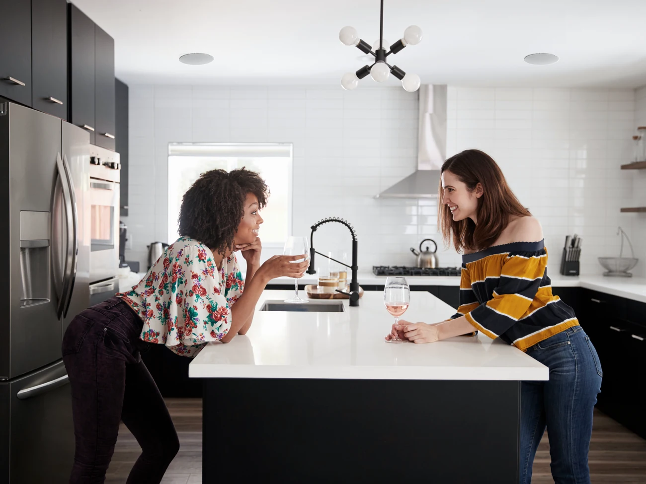 Two people talking across a kitchen island, with a Lithe Audio speaker set into the ceiling
